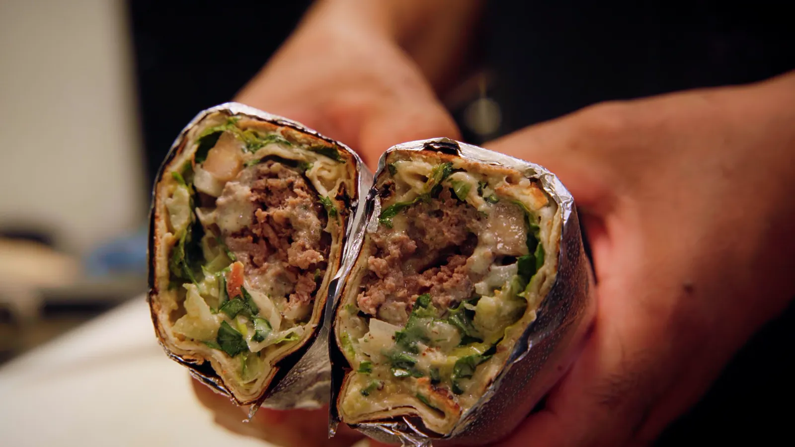 An Adana kebab wrap cut in half, showing the kebab, greens and sauce inside