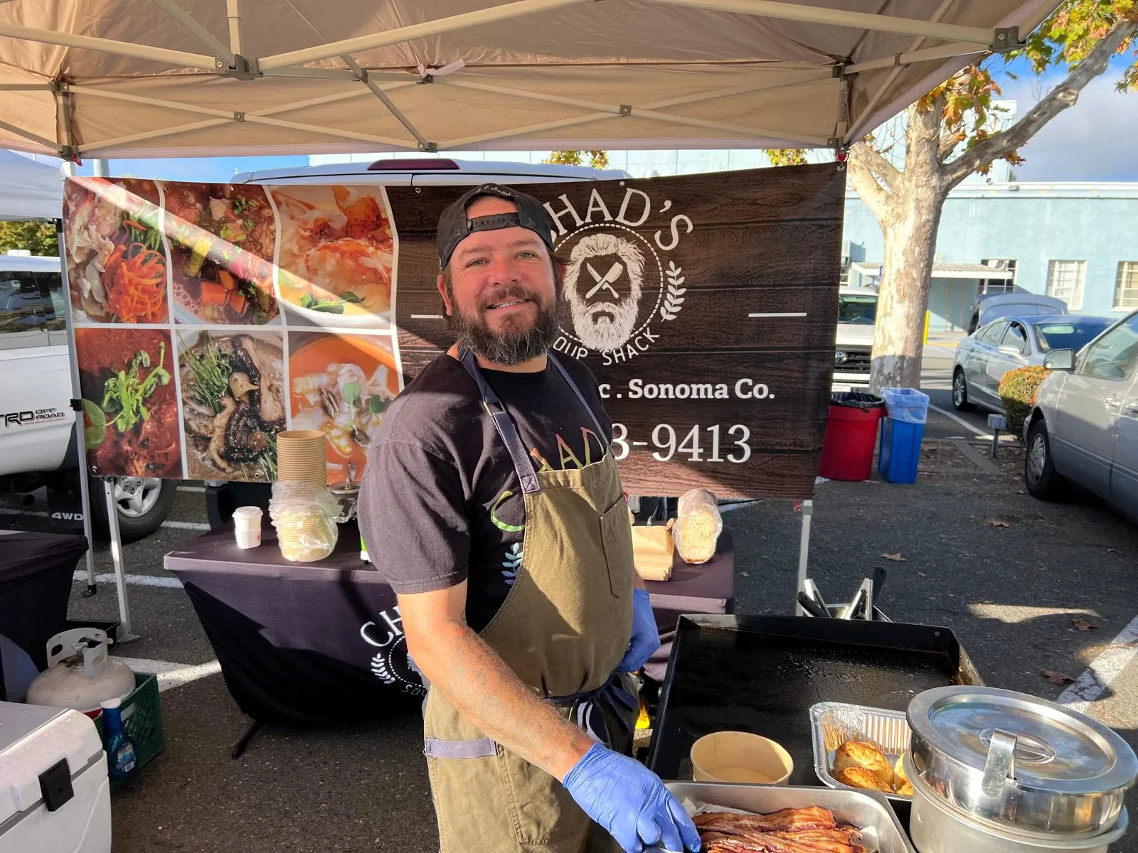 Chad's Soup Shack stand with a flat-top griddle, bacon and a banner covered in soup photos