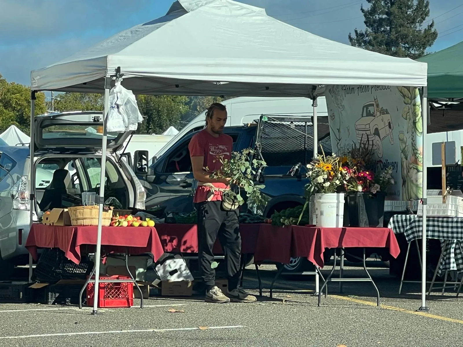 A farm stand with buckets of flowers, eucalyptus and apples under a white tent