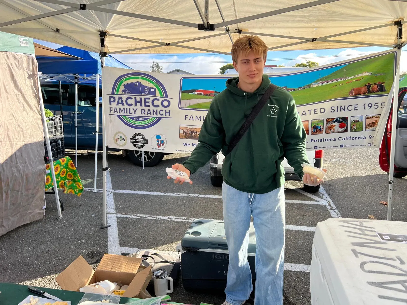 A young man at the Pacheco Family Ranch stand holding butter in one hand and cheese in the other